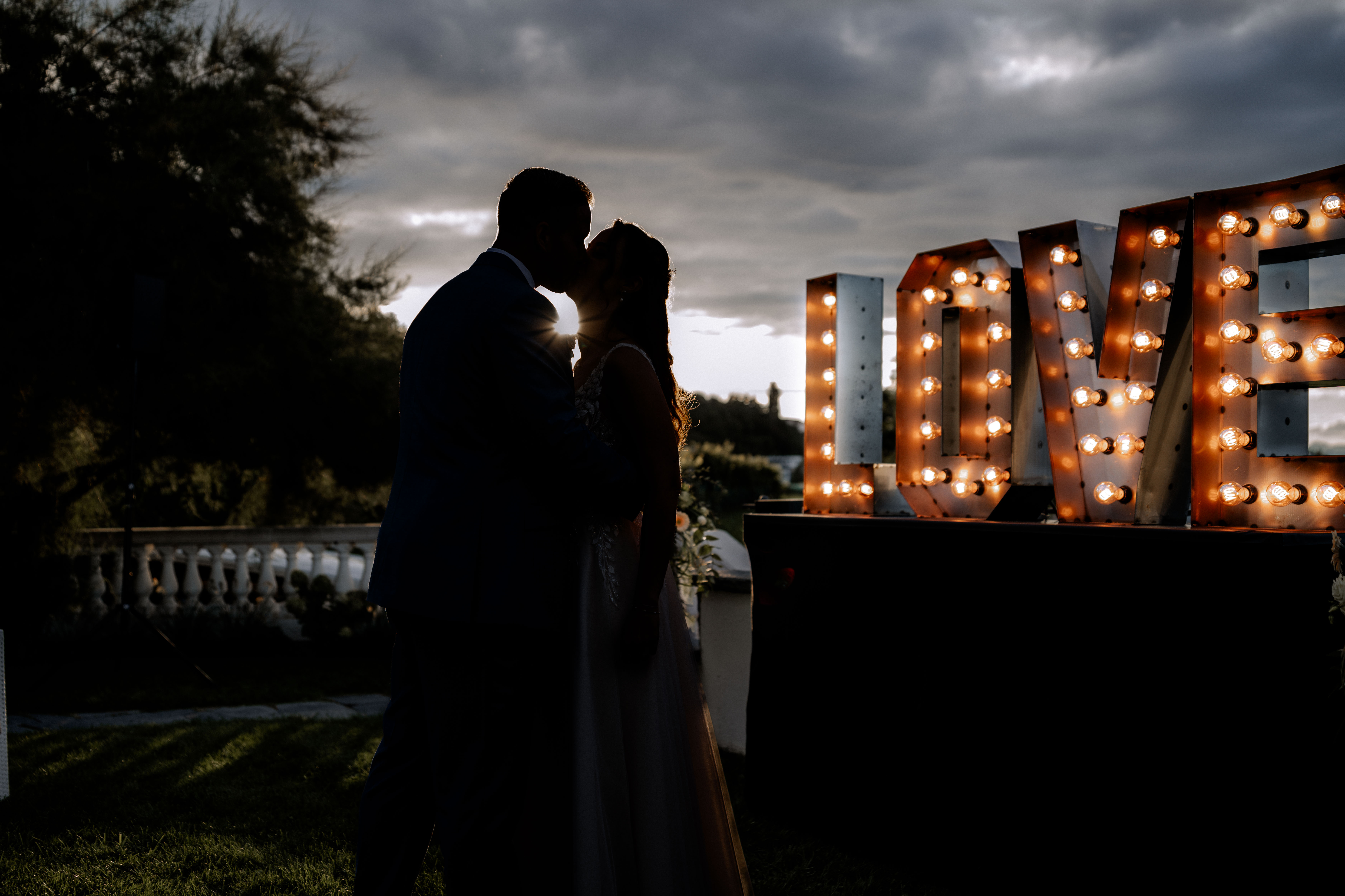 Brautpaar küsst sich vor beleuchteten LOVE-Buchstaben bei Sonnenuntergang. Hochzeitsfotografie. - Hochzeitsfotograf Pablo aus Thurgau